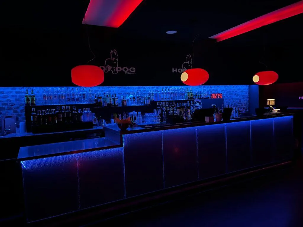 Bar gay Milano con luci blu e rosse, atmosfera di locale notturno underground.